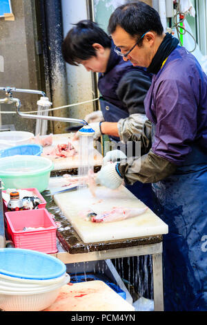 Kuromon Ichiba, Osaka's kitchen food market. Two men, standing while slicing fish up, working on table with running water flowing off the end. Stock Photo