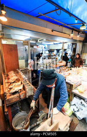 Kuromon Ichiba, Osaka's kitchen food market. Fish mongers, interior, sea beams cooking over bricked barbeque, background, cluttered boxes of fish. Stock Photo