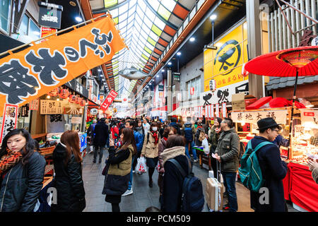Kuromon Ichiba, Osaka's kitchen food market. View along arcade with various stalls and shops on both sides of arcade. Busy with people, crowded. Winte Stock Photo