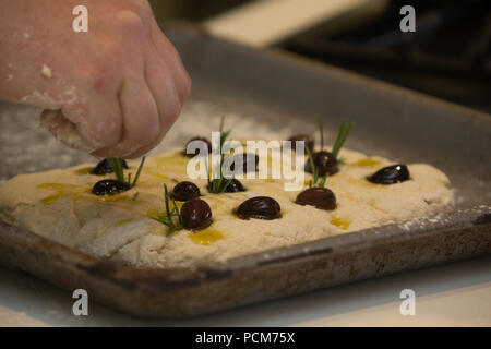 A hand placing olives and herbs on soda bread focaccia dough Stock Photo