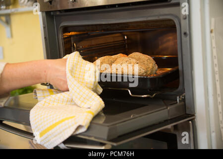 A hand using a dish towel to take a loaf of Irish brown bread out of the oven. Stock Photo