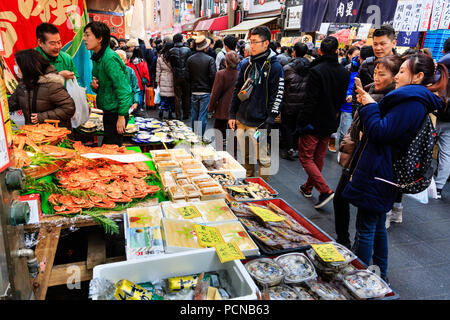 Kuromon Ichiba, Osaka's kitchen food market. Seafood stall with two people talking cellphone picture of orange crabs. Market very crowded, wintertime. Stock Photo