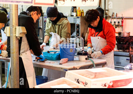 Kuromon Ichiba, Osaka's kitchen food market. Four men, standing while slicing fish up, working on table with running water flowing off the end. Stock Photo