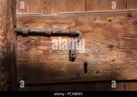 an ancient rusted metallic lock and latch system on a wooden door from the middle ages located in an abandoned mountain village in northern Italy Stock Photo