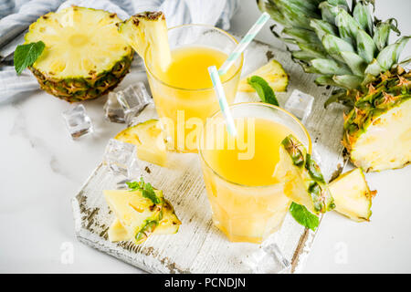 Fresh pineapple juice or cocktail, with pieces of fresh pineapple, ice, decorated with mint, on a white marble table, copy space Stock Photo