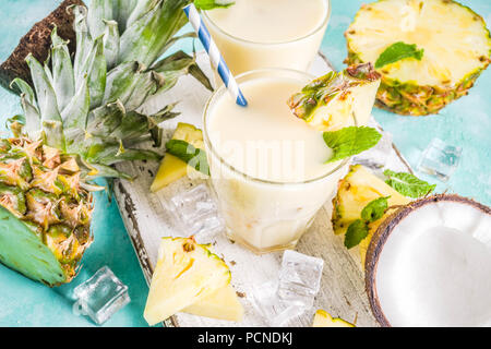 Refreshing summer drink, homemade pina colada cocktail, on a light blue background, with pieces of pineapple, coconut, ice and mint leaves, copy space Stock Photo