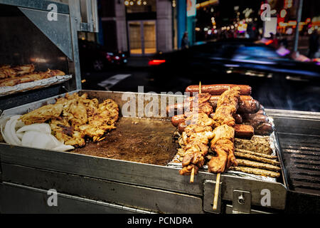 A grill at a food stand in New York City with chicken, sausages and kebabs on skewers. Stock Photo