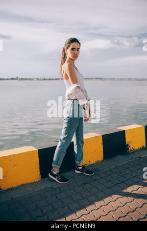 https://l450v.alamy.com/450v/pcnen9/full-body-portrait-of-beautiful-girl-standing-near-the-sea-at-sunny-summer-day-teen-female-wearing-boyfriend-jeans-and-white-top-posing-at-city-port-pcnen9.jpg