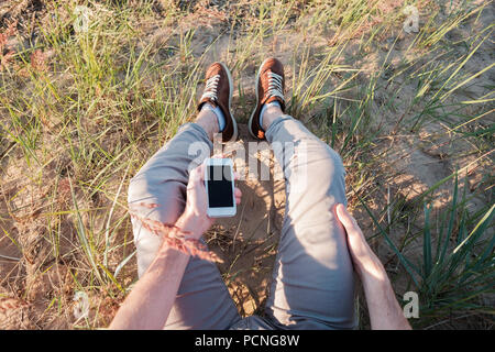 Outdoor photo of man sitting on grass holding phone with blank screen. Concept of being in contact every moment in a day Stock Photo