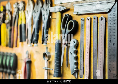Tools and devices hanging on workshop wall. Rulers, cutting knives, scissors and other objects well arranged in working place. Stock Photo