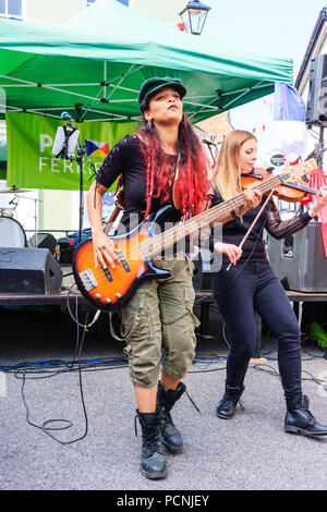 Musician Reden Rock on bass guitar and woman on violin, of folk rock band Triskelles performing in open air concert. Low angle view, facing. Stock Photo