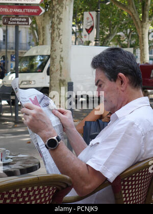 Man relaxing whilst sitting outside french street cafe reading a newspaper Stock Photo