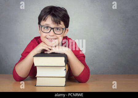smiling little boy leaning on books on a table on black background Stock Photo