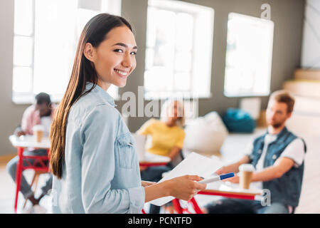 young asian student girl with paper standing in front of classmates and looking at camera Stock Photo