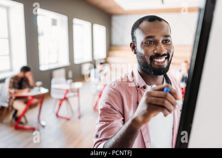 happy young african american teacher writing on whiteboard at lecture room with blurred students sitting on background Stock Photo