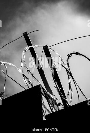 Close up of barbed wire, razor wire, barbwire on the cloudy sky in black and white colors Stock Photo