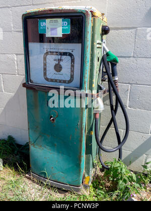 Disused green decaying petrol pump against a cinder block white painted wall Stock Photo