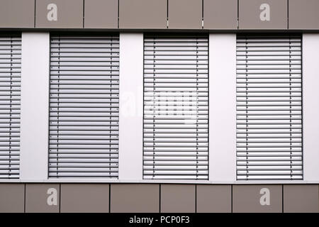 The modern facade of an office building with rows of windows and metal blinds.