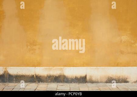 Yellow old faded wall and empty sidewalk with stone detail Stock Photo