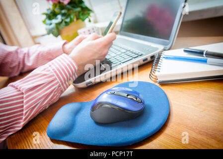 Man working at home office using smart phone and laptop, computer mouse in a foreground Stock Photo