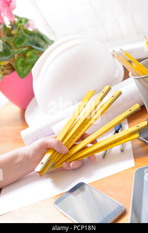 Construction plans in hand with helmet, measure, mobile phone, and drawing tools Stock Photo