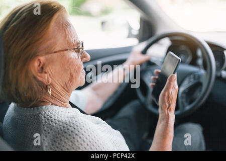 Elderly woman behind the steering wheel of a car using her phone Stock Photo