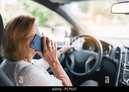 Elderly woman behind the steering wheel of a car using her phone Stock Photo