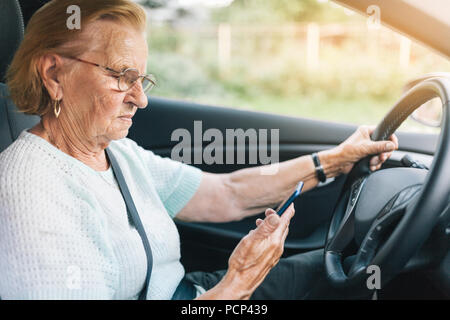 Elderly woman behind the steering wheel of a car using her phone Stock Photo