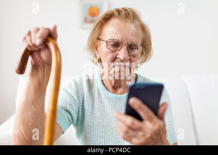 Elderly woman with glasses and cane using a mobile phone Stock Photo