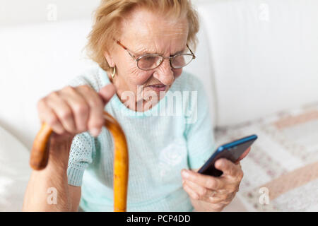 Elderly woman with glasses and cane using a mobile phone Stock Photo