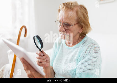 Elderly woman with glasses and loupe using a modern digital tablet Stock Photo