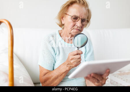 Elderly woman with glasses and loupe using a modern digital tablet Stock Photo