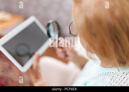 Elderly woman with glasses and loupe using a modern digital tablet Stock Photo