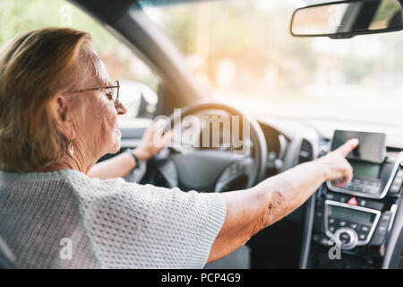 Elderly woman behind the steering wheel of a car using her satnav Stock Photo