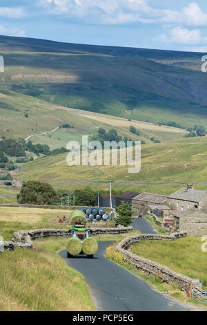 Tractor leading big bales of silage down a narrow rural road near Hoggarths in Swaledale, North Yorkshire, UK. Stock Photo