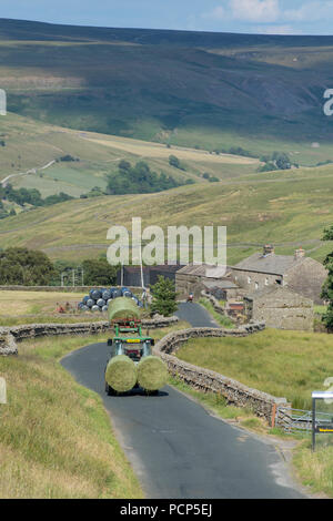 Tractor leading big bales of silage down a narrow rural road near Hoggarths in Swaledale, North Yorkshire, UK. Stock Photo