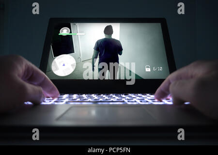 Teenage boy or young man playing action or crime video game with laptop. Computer and online gaming concept. Low close up view to hands on keyboard. Stock Photo