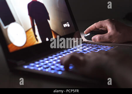 Young man playing video game with laptop. Gamer with computer in dark or late at night. Hands on mouse and keyboard. Stock Photo