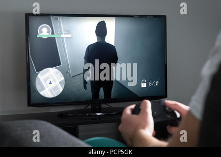 Playing video games at home with console. Gamer with controller or gamepad in hand. Young man and TV with action game on screen. Stock Photo