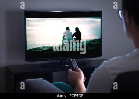 Man watching tv or streaming movie or series with smart tv at home. Film or show on television screen. Person holding the remote control. Stock Photo
