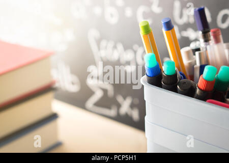 Pen holder and books in front of blackboard in classroom. Education, learning, teaching and knowledge concept. Classroom with chalkboard. Stock Photo