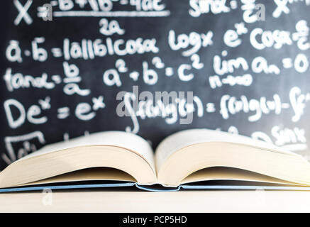 Knowledge, education, mathematics, science and wisdom concept. Open book in front of a blackboard and chalkboard full of math writing. Stock Photo