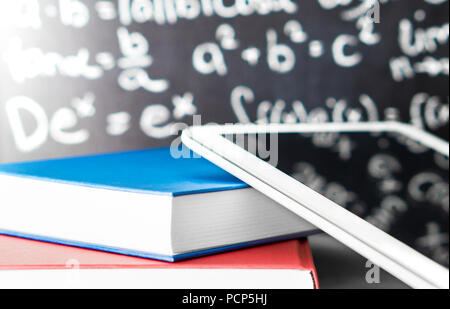 E learning and modern education concept. Smart mobile device and tablet with stack of colorful books in front of a blackboard in school. Stock Photo