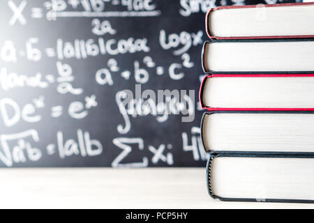Stack and pile of books in front of a blackboard in school. Math equation handwritten on chalkboard. Stock Photo