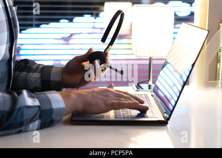 Call center, 24/7 help desk or support hotline concept. Video call conference or telemarketing. Customer service person holding headset late at night. Stock Photo