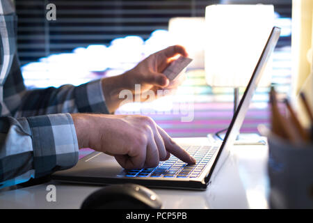 Online shopping and paying with credit card and laptop. Man buying on an internet store in modern home office late at night. Typing login information, Stock Photo