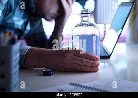 Alcoholism or drinking problem concept. Alcoholic with vodka bottle on table. Man and alcohol late at night. Drunk at work or in home office. Stock Photo