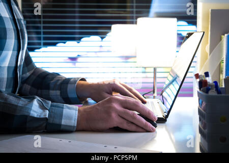 Working late at night, overtime or overwork concept. Man using laptop in modern business office with blurred city background. Stock Photo
