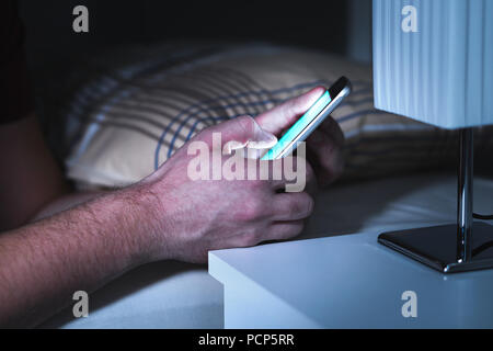 Man using smartphone in bed late, in the middle of the night. Mobile phone in bedroom. Texting or using social media. Cellphone addiction. Stock Photo