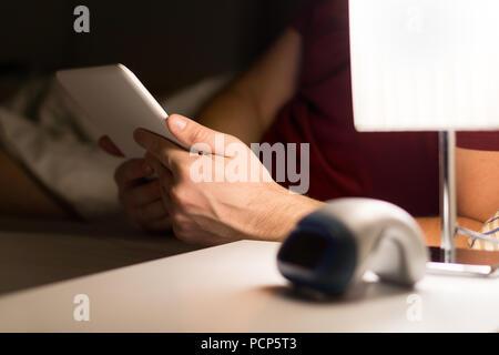Man reading electronic book or using tablet in bed. Modern mobile device in hand in bedroom. Watching movies or series online before going to sleep. Stock Photo